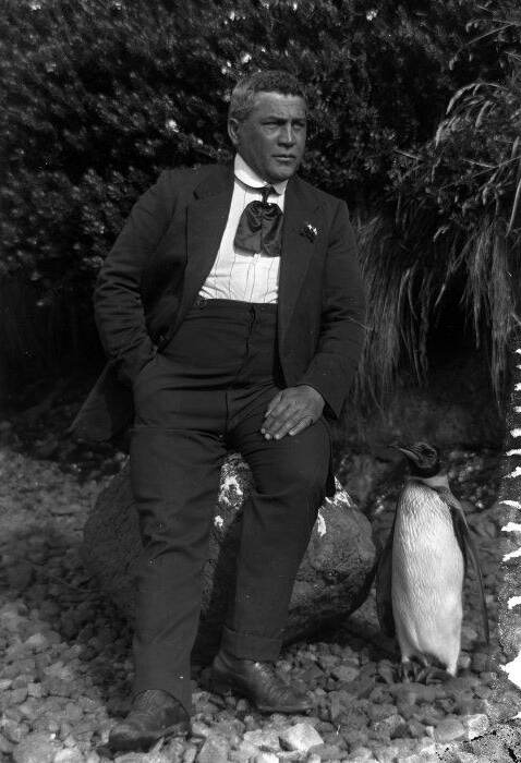 Jack Norton seated in his suit with a king penguin standing beside him