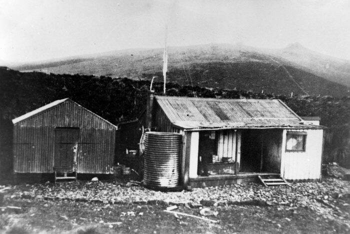 Two corrugated iron huts and a water tank below the hills at Tucker Cove