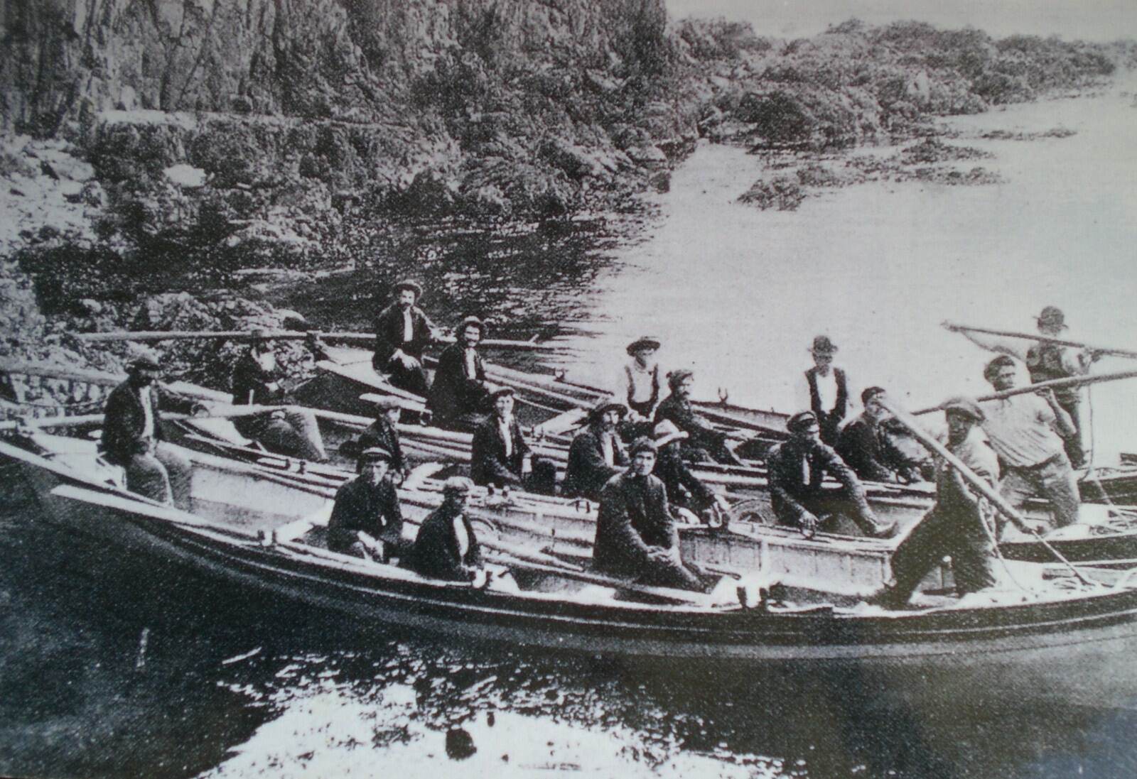 Open whaleboats crowded with men under the cliffs at the Tory Channel lookout
