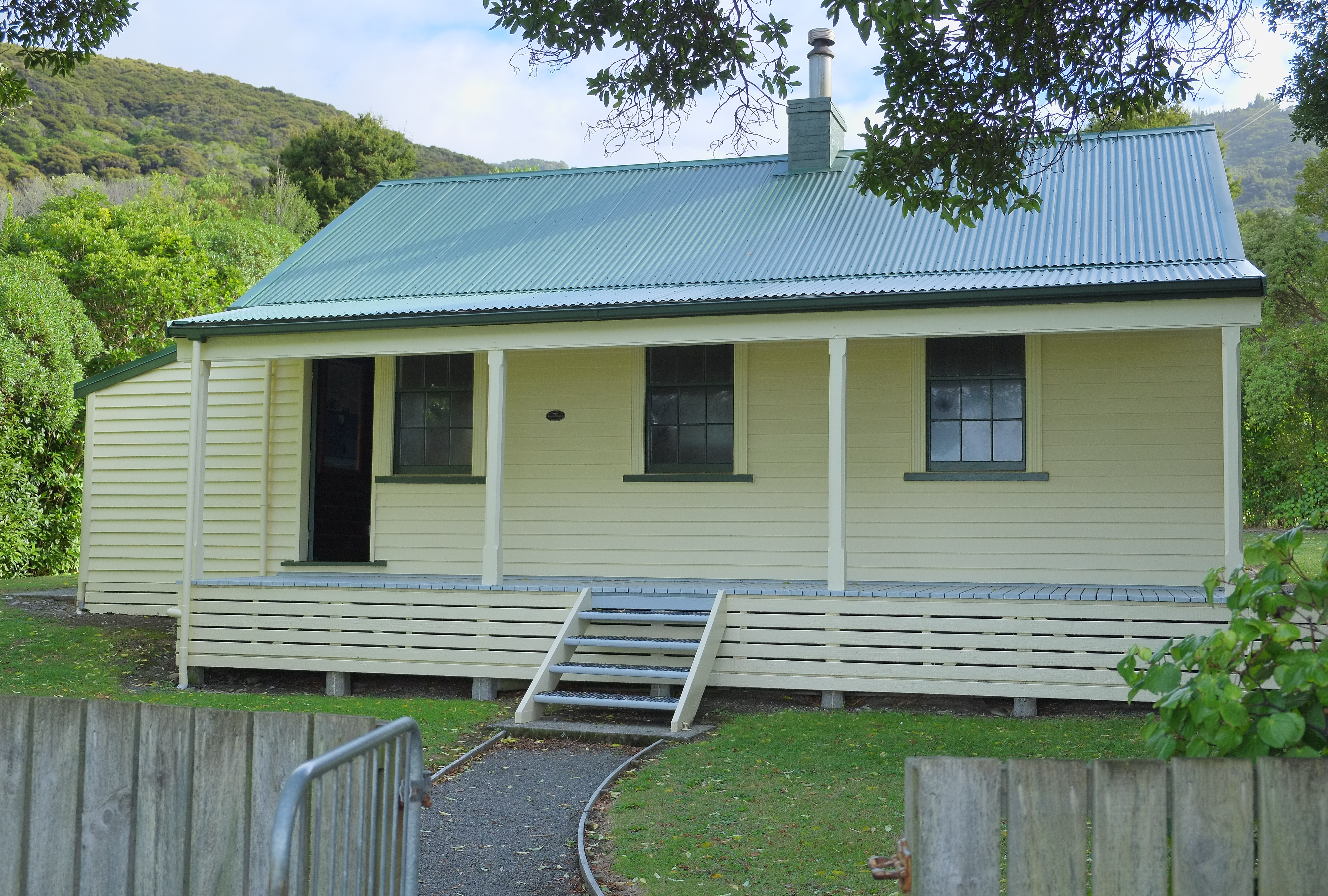 The surviving White’s Bay cable-station building, with pale weatherboards, green roof and veranda.